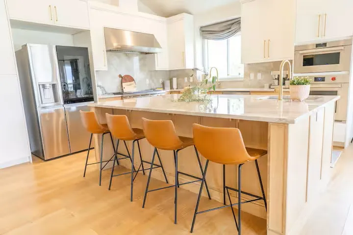 Gourmet kitchen featuring a large central island with seating, stainless steel appliances, light wood-finish flooring, white cabinetry, and a light-toned countertop
