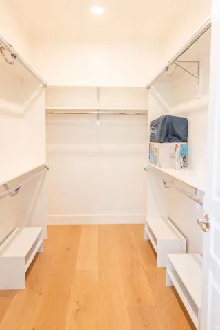Walk-in closet featuring wood-finish flooring, recessed lighting, multiple shelving tiers, and integrated hanging rods