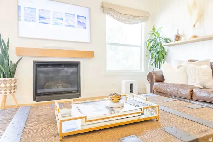 Living area featuring a fireplace with a wood mantle, a window with a Roman shade, a built-in floating shelf, and wood-finish flooring