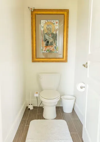 Compact water closet featuring wood-finish flooring, white baseboards, and a solid core door with brushed nickel hardware
