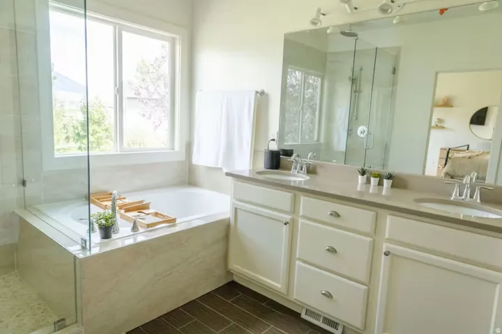 Spacious bathroom featuring a dual vanity with light-toned countertops, an integrated soaking tub, and a separate glass-enclosed shower
