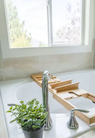 White built-in bathtub featuring a chrome faucet with dual handles, set within a tiled surround, under a white-framed window