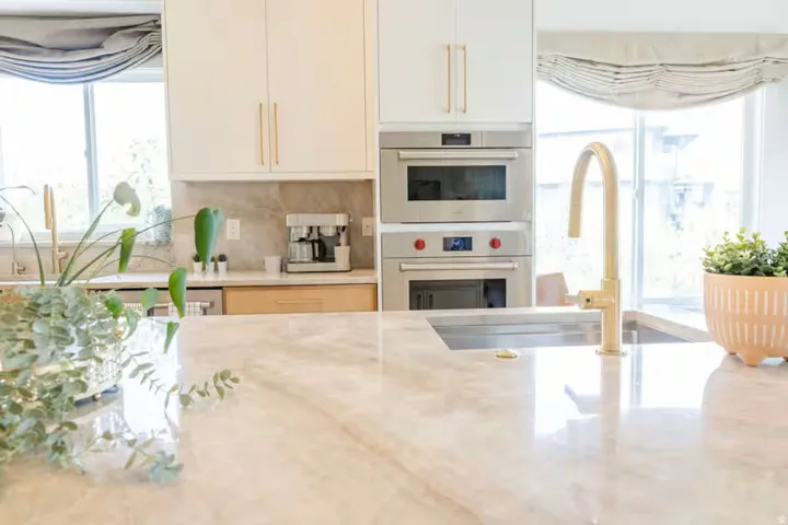 Spacious kitchen featuring a large island with a built-in sink, gold-finish faucet, and light-toned, veined countertop