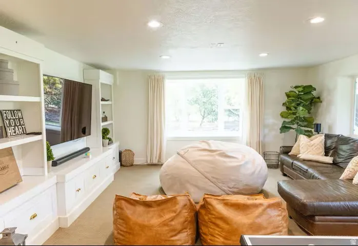 Spacious living area featuring extensive built-in cabinetry with shelving, recessed lighting, and a large window with privacy drapes