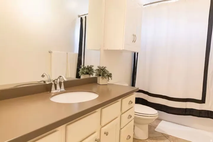Bathroom with tile flooring, a built-in vanity featuring a light brown countertop and white cabinetry, a large mirror, and an overhead white cabinet