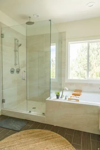 Bathroom featuring a glass-enclosed shower with dual shower heads, a built-in soaking tub with a deck-mounted faucet, large format wall tiling, and wood-finish floor tiles