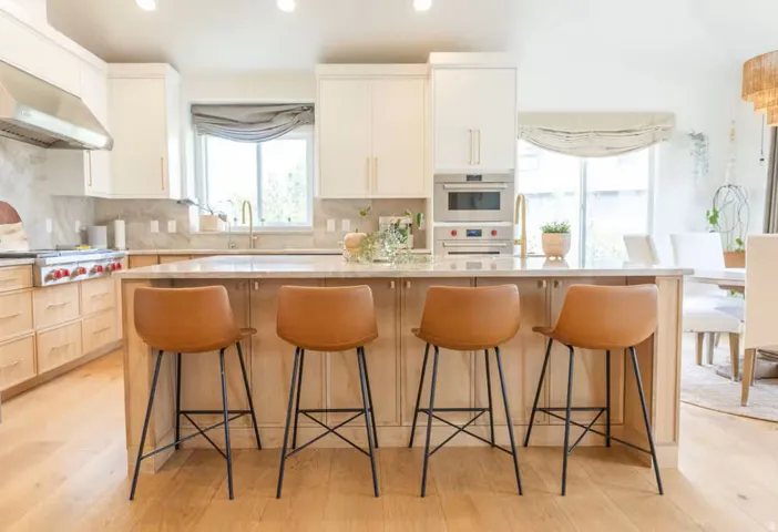 Kitchen featuring a large island with seating, integrated sink with brass faucet, light wood-finish flooring, white upper cabinetry, and light wood-finish lower cabinetry