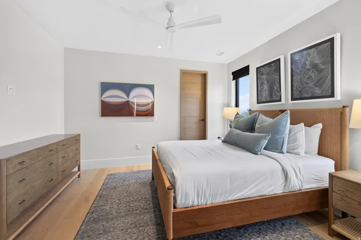 Spacious bedroom featuring light wood-finish flooring, a contemporary ceiling fan, and a light-colored solid wood door