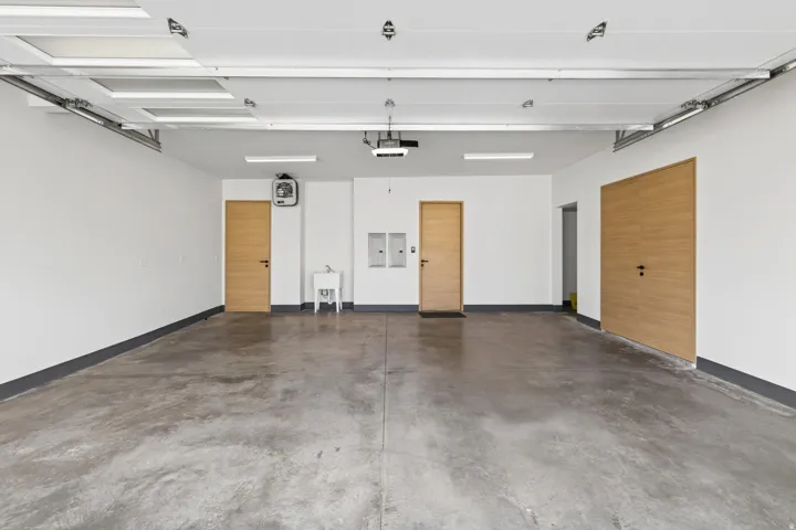Spacious garage featuring a concrete floor, bright overhead lighting, three wood-finish doors, and a utility sink