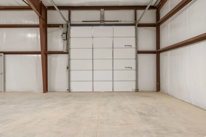 Spacious interior featuring a large white sectional overhead door, exposed metal beam construction, insulated walls, and a concrete floor