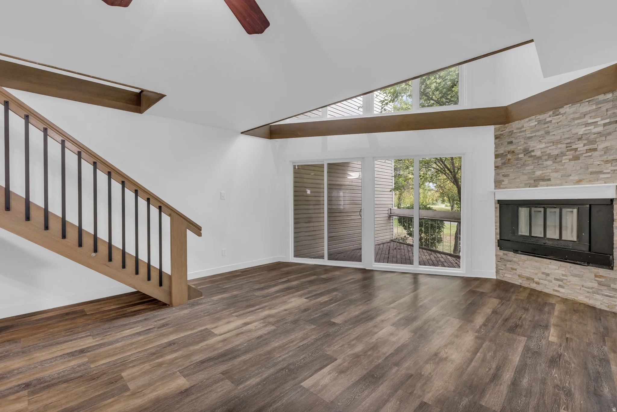 Living area featuring wood-finish flooring, a stone fireplace, vaulted ceilings with exposed beams, and a sliding glass door opening to an outdoor deck