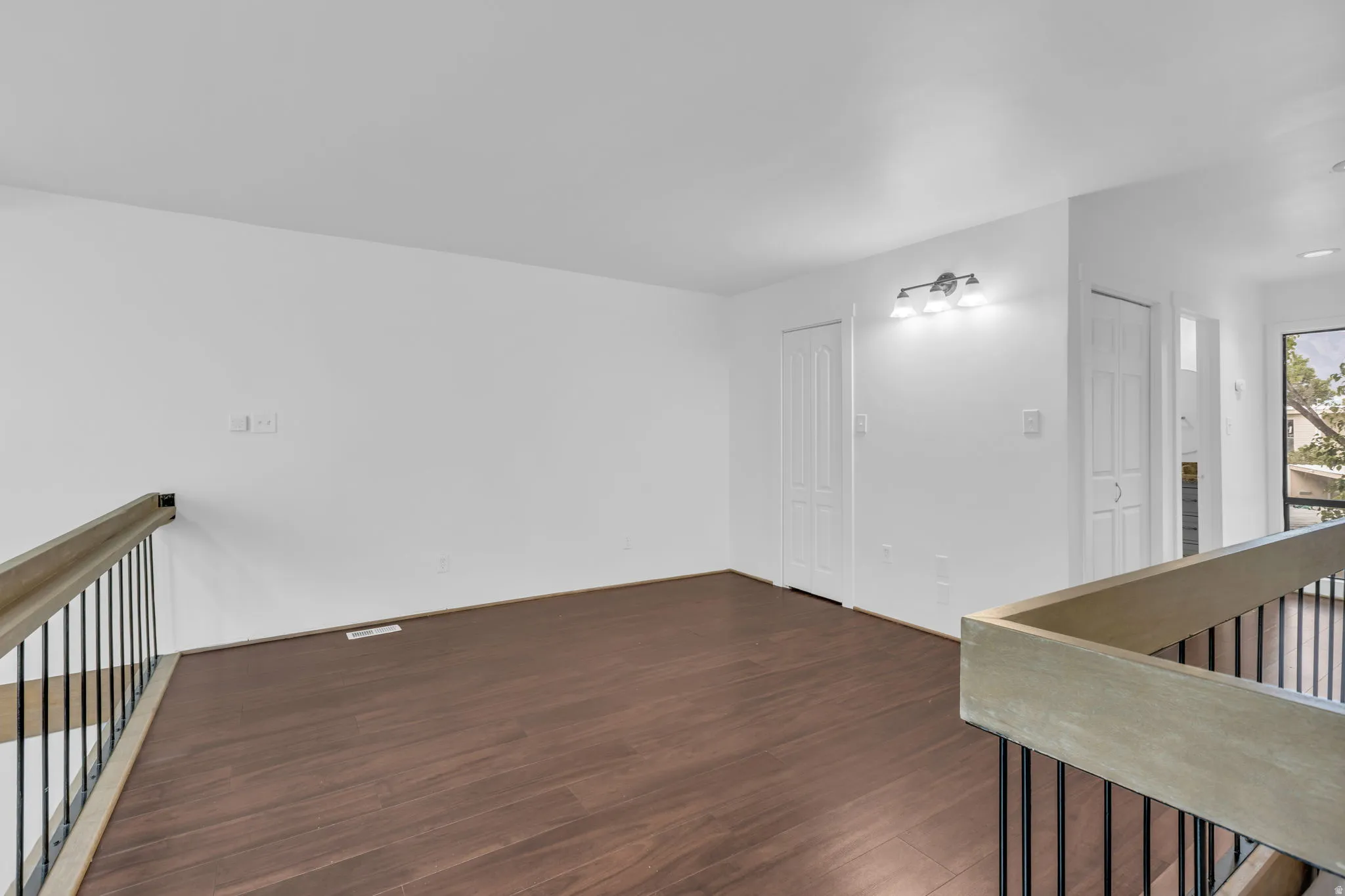 Spacious loft area featuring dark wood-finish flooring, white walls, and a contemporary three-light fixture