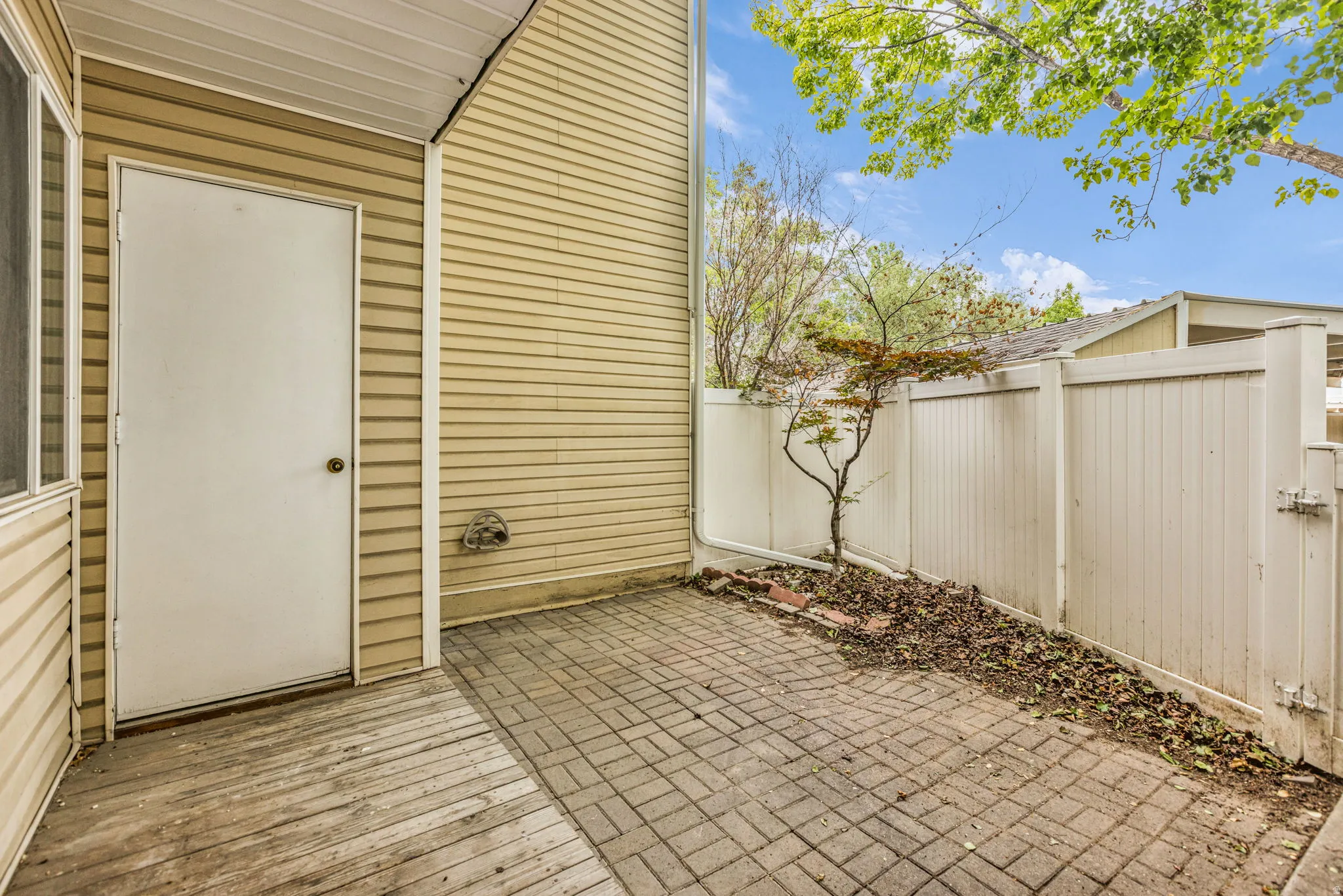 Outdoor patio area featuring textured siding, a white service door, wood-finish decking, and brick paver flooring