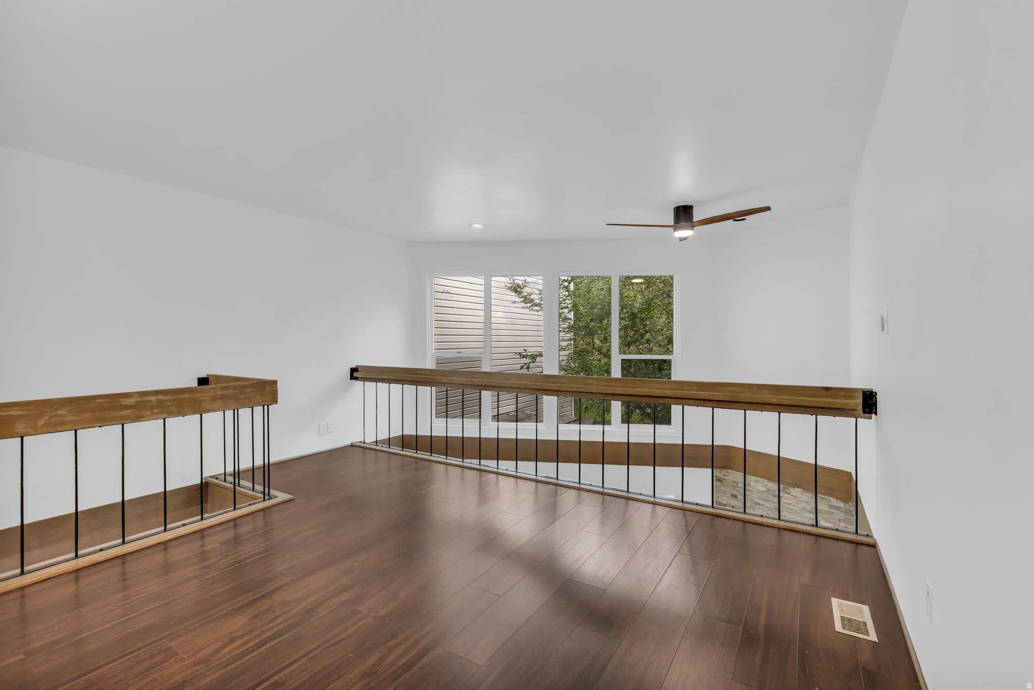 Open loft space featuring wood-finish flooring, white walls, and a modern ceiling fan
