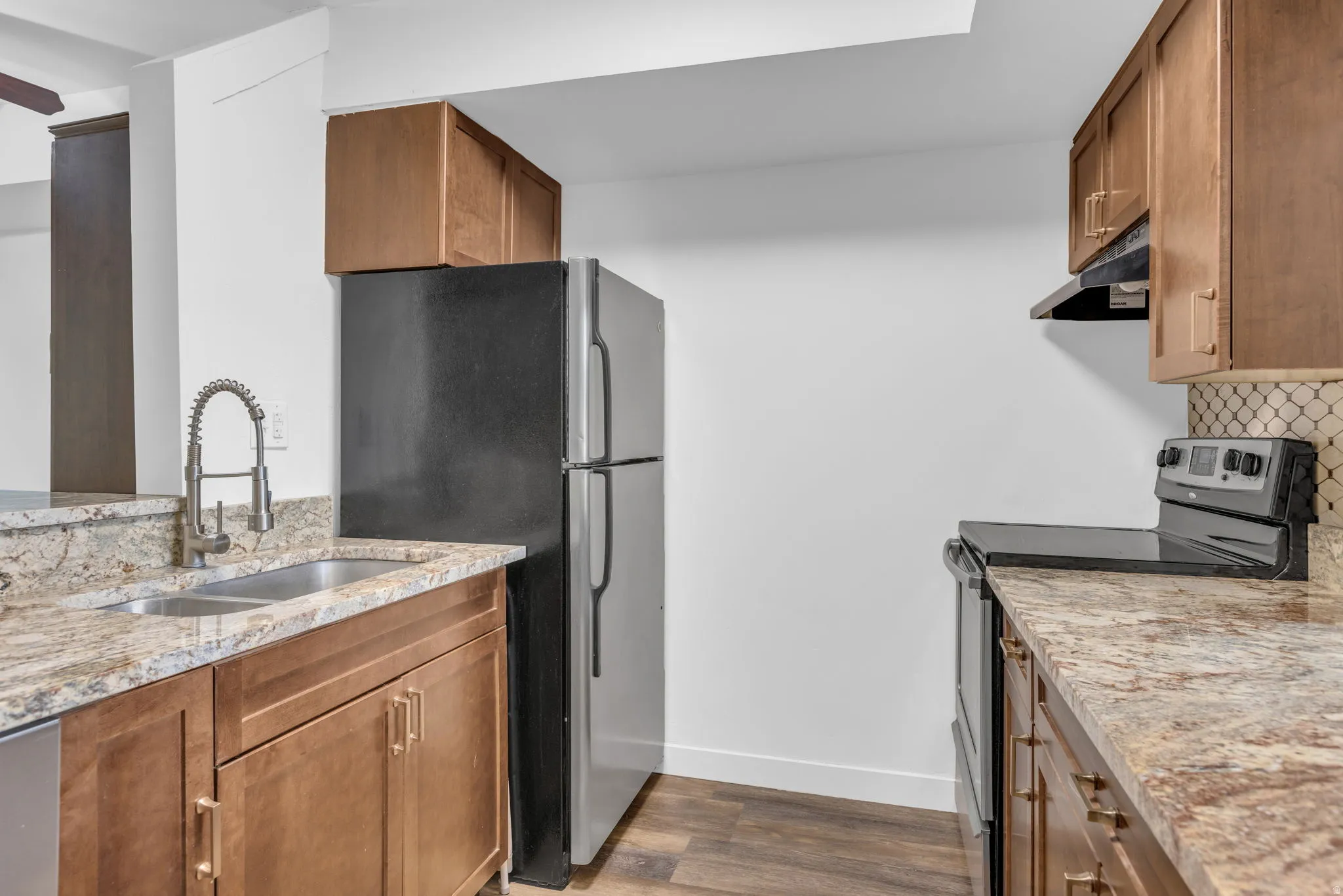 Well-appointed kitchen featuring light wood-finish cabinetry, granite-style countertops, stainless steel appliances, a double basin sink with a gooseneck faucet, and wood-finish flooring