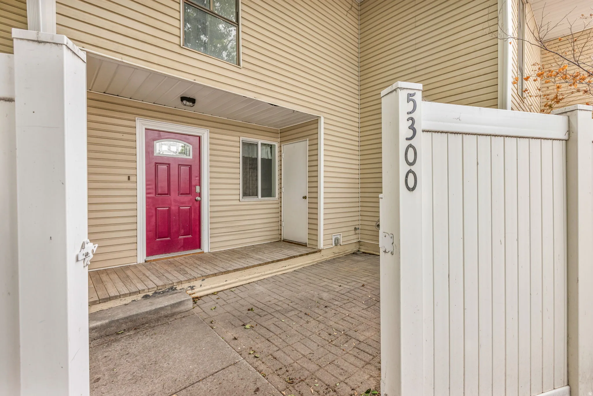 Inviting entryway featuring a vibrant red four-panel door with decorative glass, sheltered by a covered porch with wood-finish decking