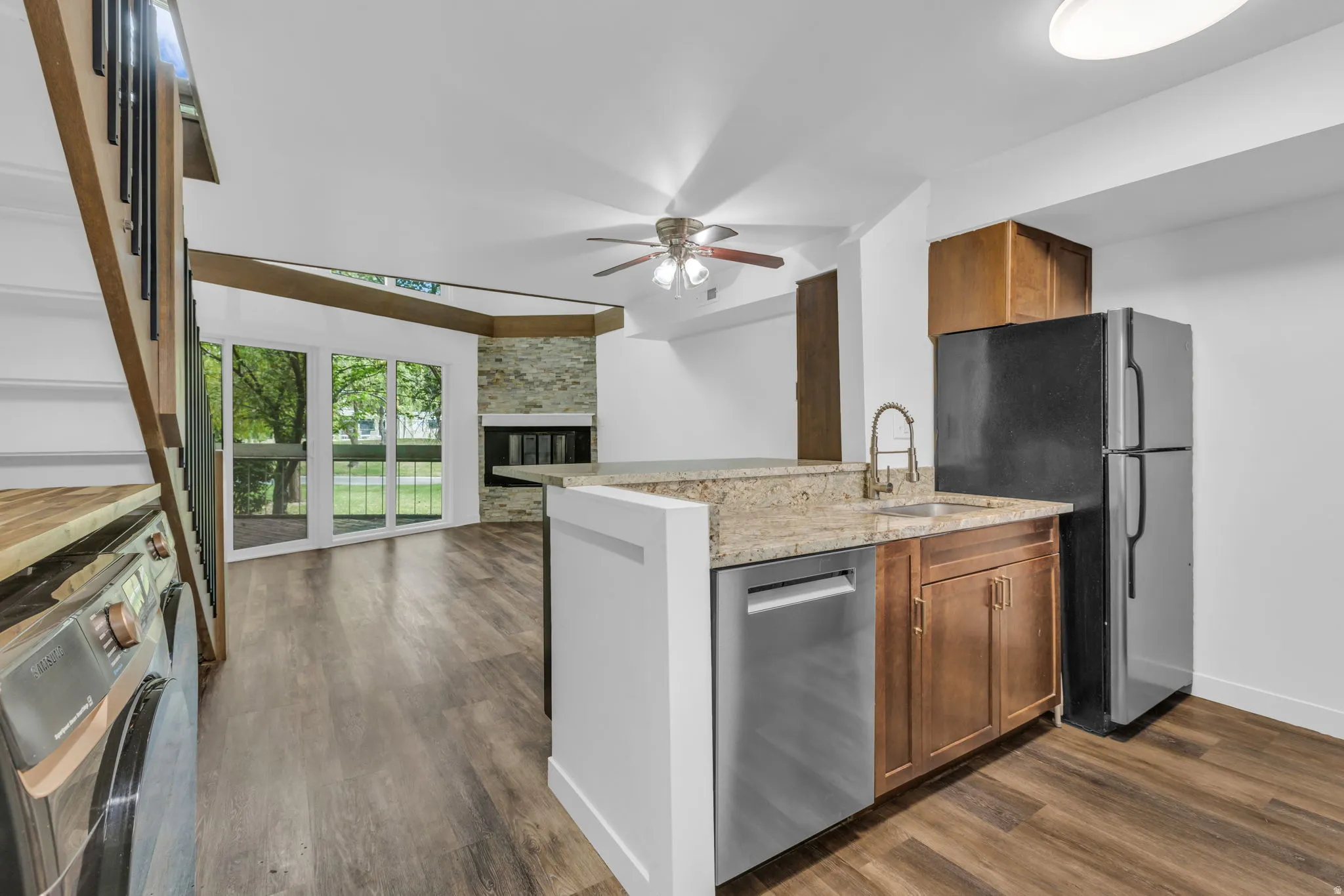 Open-concept living area featuring wood-finish flooring, a stone-clad fireplace, and sliding glass doors