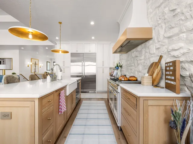 Gourmet kitchen featuring a stone accent wall, professional-grade range, full-size stainless steel refrigerator, white shaker cabinetry, and a large central island with a farmhouse sink