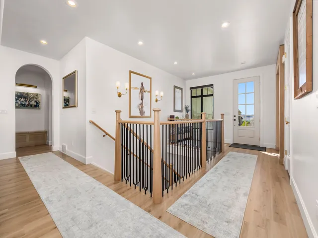 Upper-level landing featuring wood-finish flooring, recessed lighting, and a staircase with a wood handrail and black metal balusters