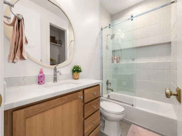Bathroom featuring a wood-finish vanity with a white countertop, an undermount sink, and a large oval mirror