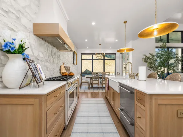 Gourmet kitchen featuring a built-in range, stone accent wall, custom wood cabinetry, and a large central island with an integrated farmhouse sink and dishwasher
