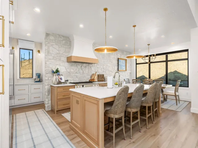 Spacious kitchen featuring a large central island with seating, a stone accent wall, light wood-finish flooring, and recessed lighting