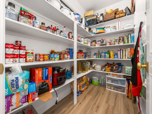 Spacious pantry featuring extensive built-in shelving, light wood-finish flooring, and white walls
