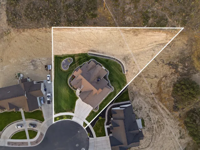 Aerial perspective highlighting a large residential lot with a manicured lawn, paved driveway, and established landscaping