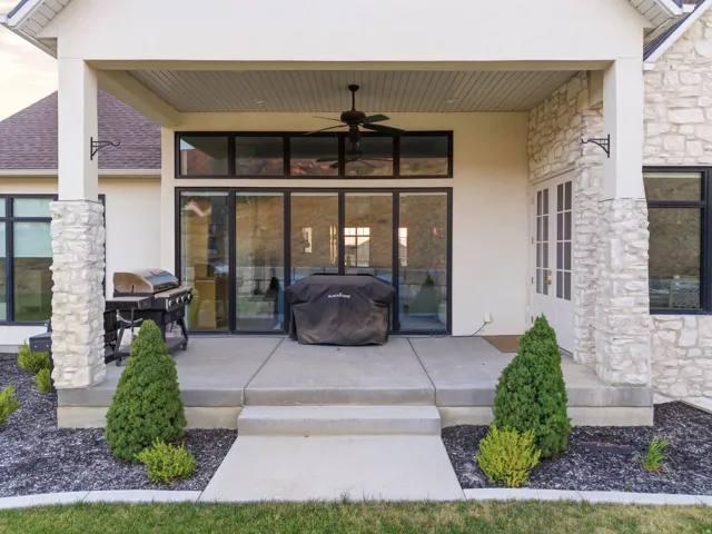 Covered outdoor patio featuring a ceiling fan, stone-clad columns, large glass sliding doors, and a French door entry