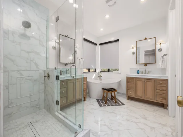 Spacious bathroom featuring a glass-enclosed shower with marble-look tile, freestanding soaking tub, dual vanity with wood cabinetry, and recessed lighting