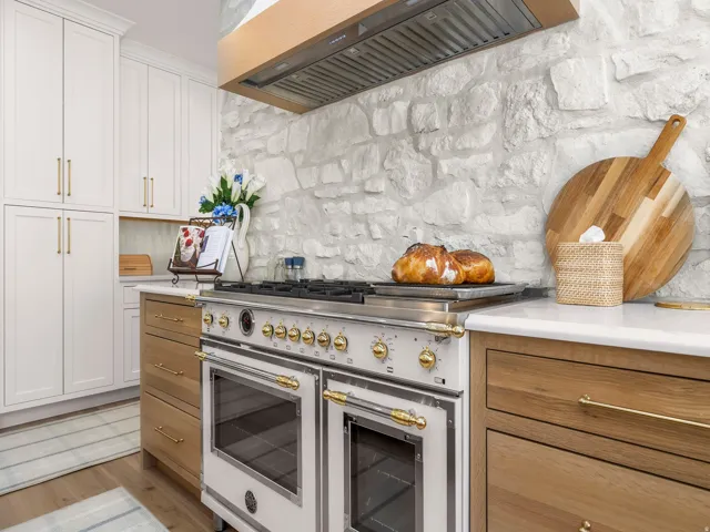 Gourmet kitchen featuring a professional-grade double oven range, stone backsplash, wood-finish cabinetry, white upper cabinetry, and white countertops