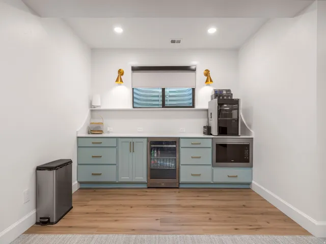 Wet bar featuring light blue cabinetry, gold hardware, a beverage refrigerator, and an integrated microwave