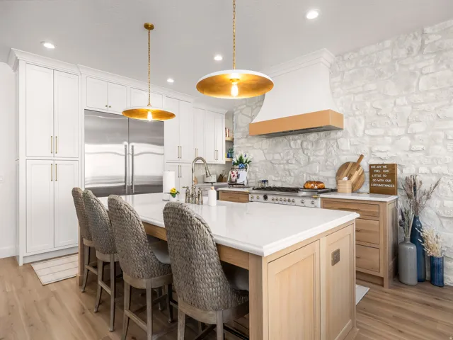 Gourmet kitchen featuring a stone accent wall, large central island with seating, stainless steel appliances, custom range hood, and wood-finish flooring