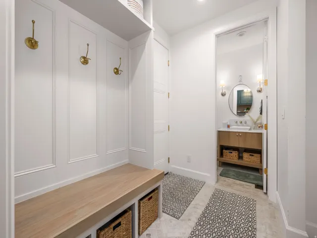 Entryway mudroom with custom built-in bench, wainscoting, and brass coat hooks