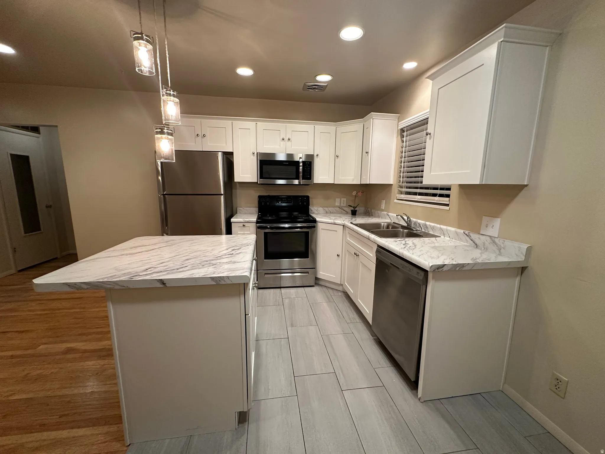 Kitchen featuring white shaker-style cabinetry, stainless steel appliances, and a breakfast bar with a white stone-look countertop