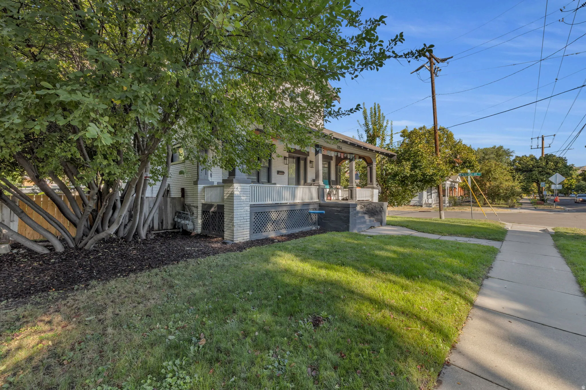 Inviting front porch with decorative railing, surrounded by mature trees and manicured lawn