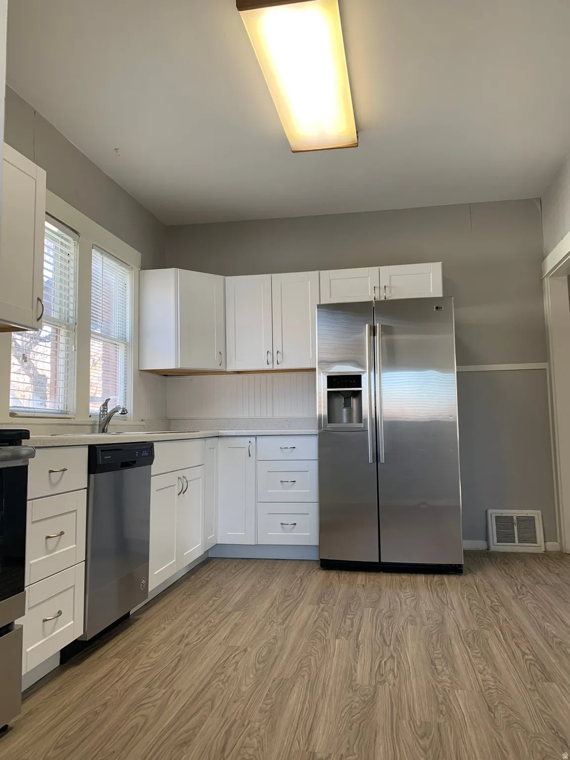 Kitchen featuring white cabinetry, wood-finish flooring, stainless steel appliances, and light-toned countertops