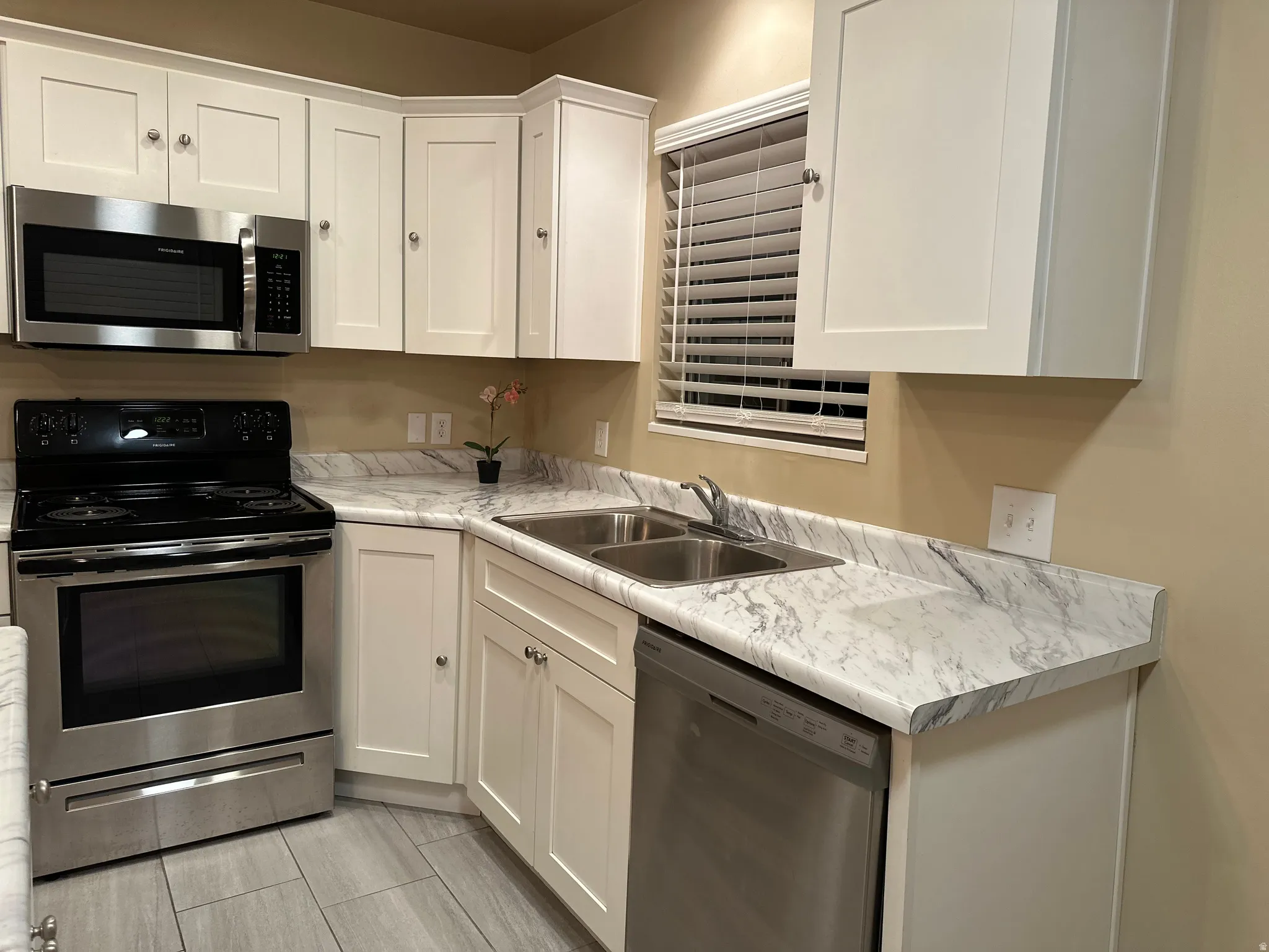 Kitchen featuring white shaker-style cabinetry, stainless steel appliances, a dual basin sink, and marbled countertops