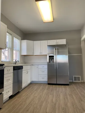 Kitchen featuring white cabinetry, wood-finish flooring, stainless steel appliances, and light-toned countertops