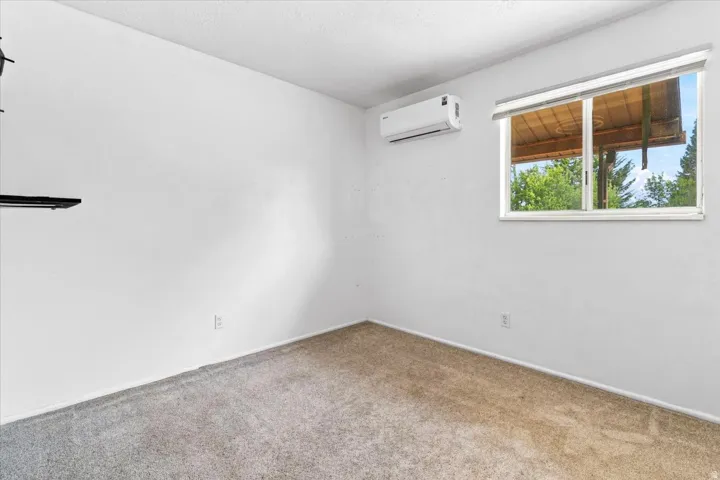 Carpeted interior space featuring white walls, a large window with white trim, and a wall-mounted mini-split HVAC unit