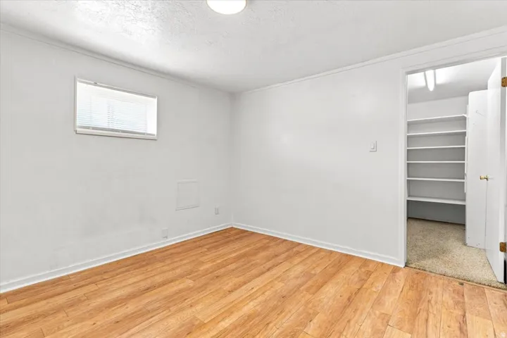 Room featuring wood-finish flooring, white walls, and a single window with blinds