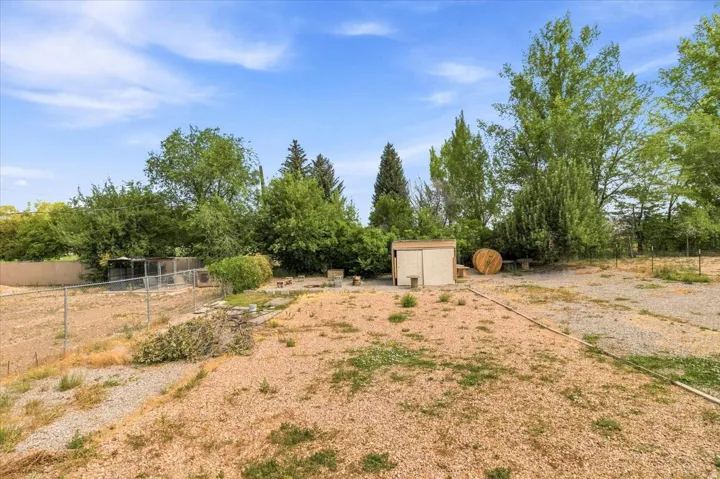 Expansive yard with a gravel and dirt surface, featuring mature trees and a detached shed