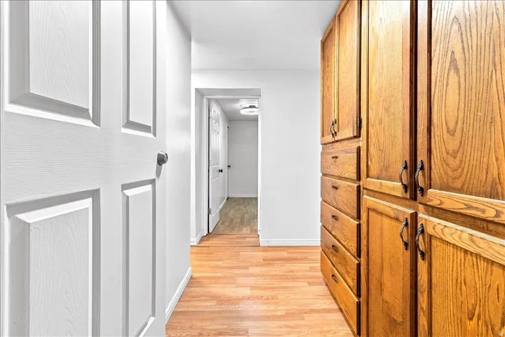Hallway featuring wood-finish flooring, white walls, and built-in wood cabinetry with dark hardware