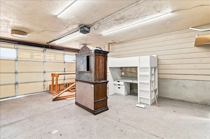 Concrete floor garage featuring an automatic garage door opener, fluorescent lighting, and horizontal wall paneling