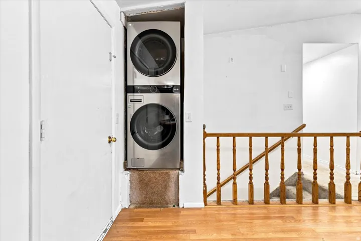 Integrated stackable washer and dryer unit, featuring stainless steel finishes, hardwood flooring, and a wooden banister