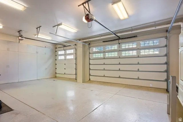 Multi-car garage featuring segmented overhead doors with transom windows, full-wall built-in cabinetry, overhead fluorescent lighting, and a sealed concrete floor
