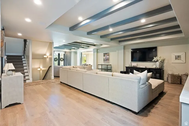 Spacious entertainment area featuring light wood-finish flooring, recessed lighting, and exposed ceiling beams