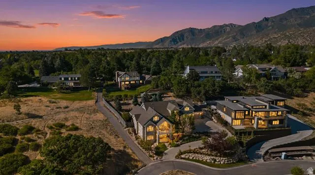 Gated community featuring a paved street, mature landscaping, and mountain backdrop