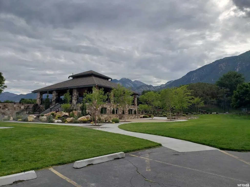 Stone-clad pavilion with a multi-tiered roofline, featuring an expansive lawn area and concrete pathways