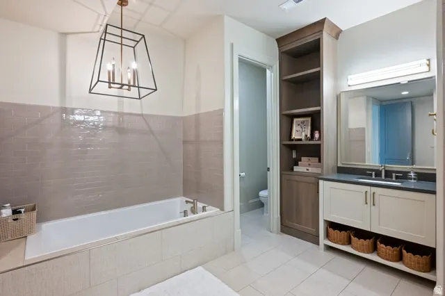 Bathroom featuring a built-in soaking tub, subway tile wainscoting, and a geometric chandelier